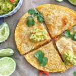 A carne asada quesadilla cut into 4s with lime wedges, cilantro, and guacamole.