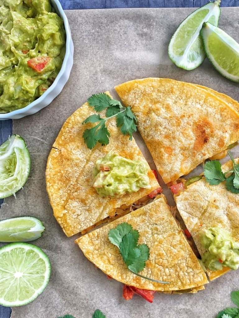A carne asada quesadilla cut into 4s with lime wedges, cilantro, and guacamole.