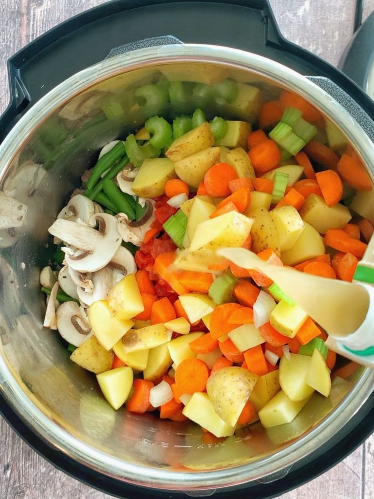 Beef broth being poured over vegetables in an Instant Pot.