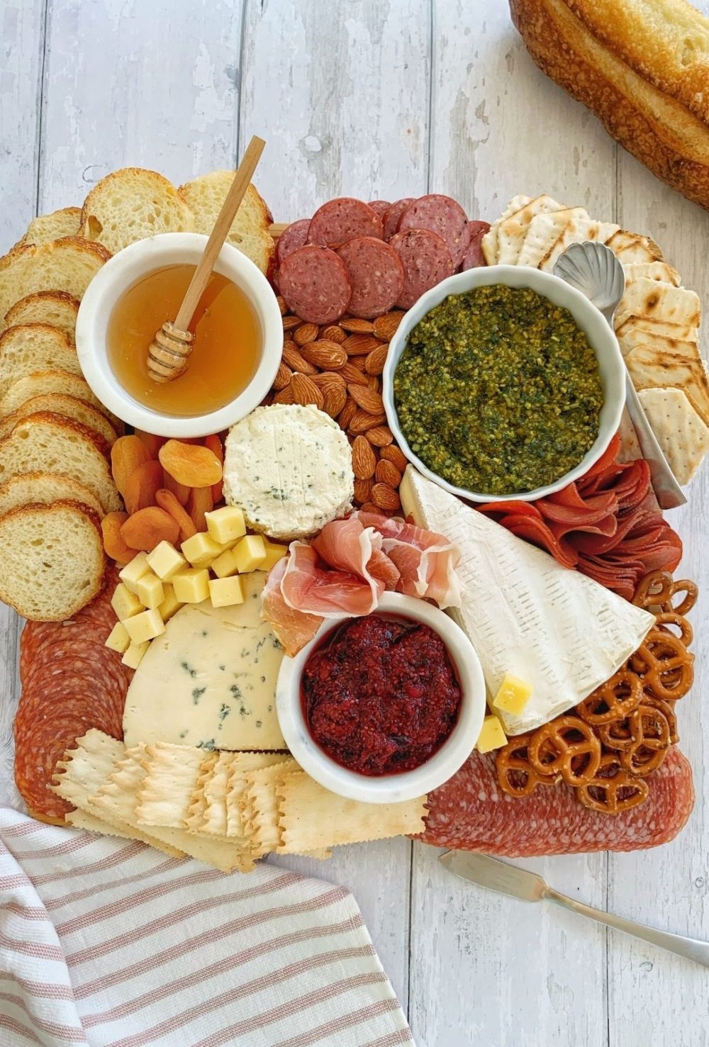 A charcuterie board full of meats, cheeses, sauces, almonds, pretzels, and bread.