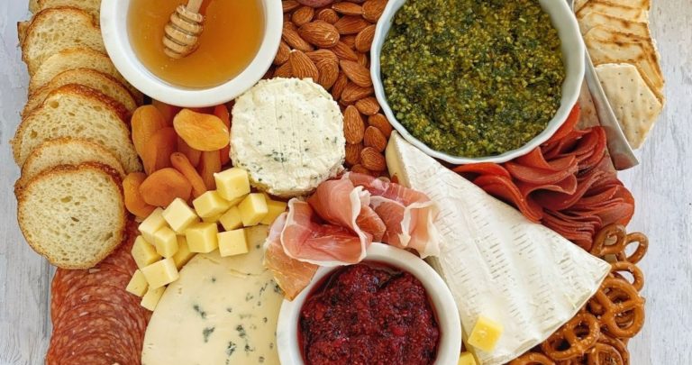 A charcuterie board full of meats, cheeses, sauces, almonds, pretzels, and bread.