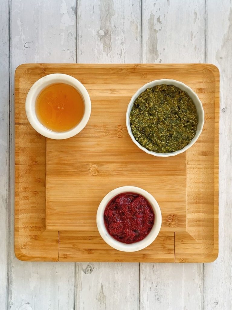 Honey, pesto, and chia seed jam in bowls on a wooded board.