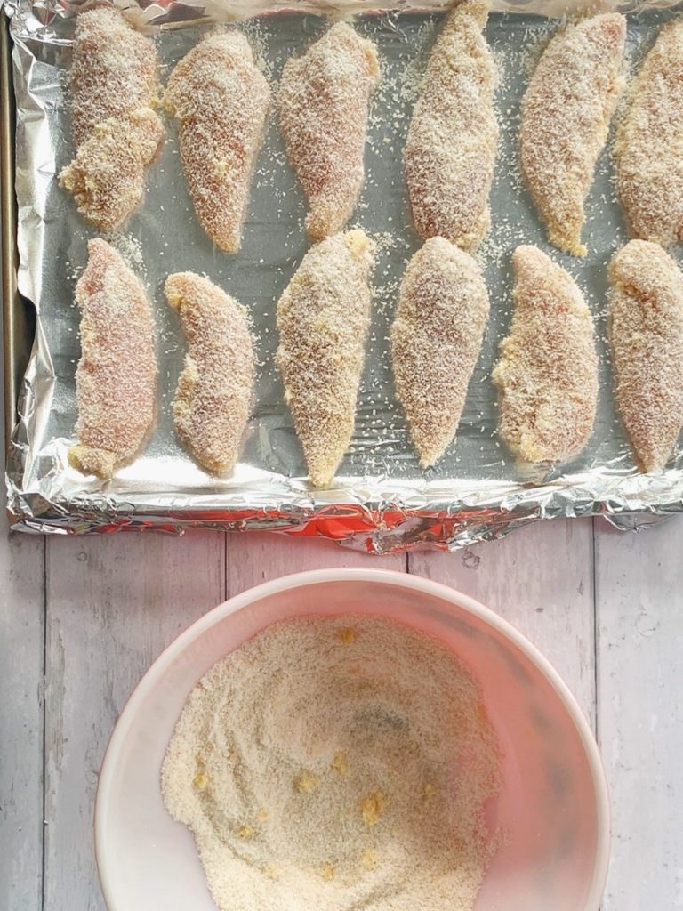 A sheet pan with coconut crusted chicken tenders arranged evenly.