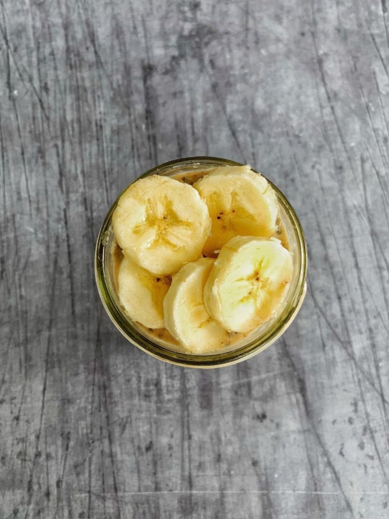 A glass jar with protein overnights oats topped with sliced banana.