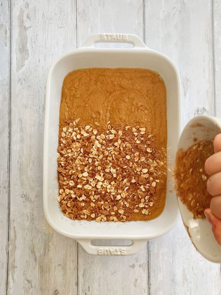 Cinnamin oat streusel being sprinkled on top of coffee cake batter in a baking pan.