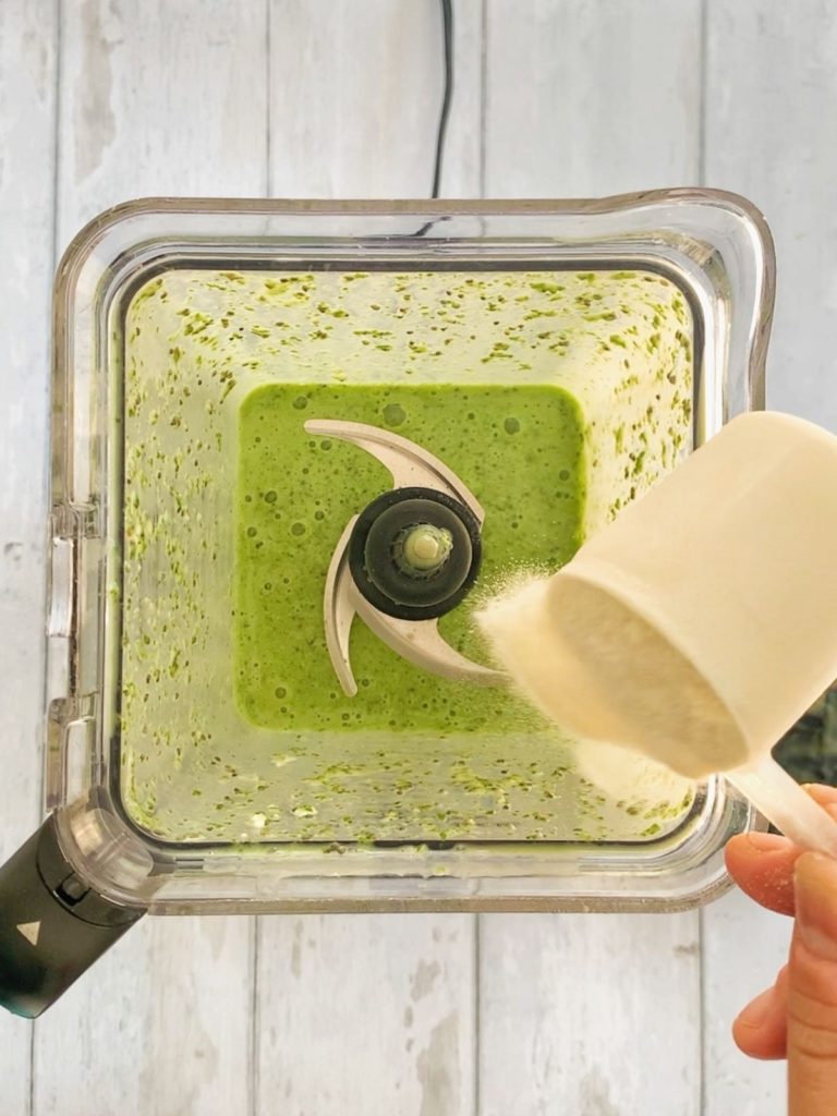 Protein powder being poured into a blender with a green smoothie.