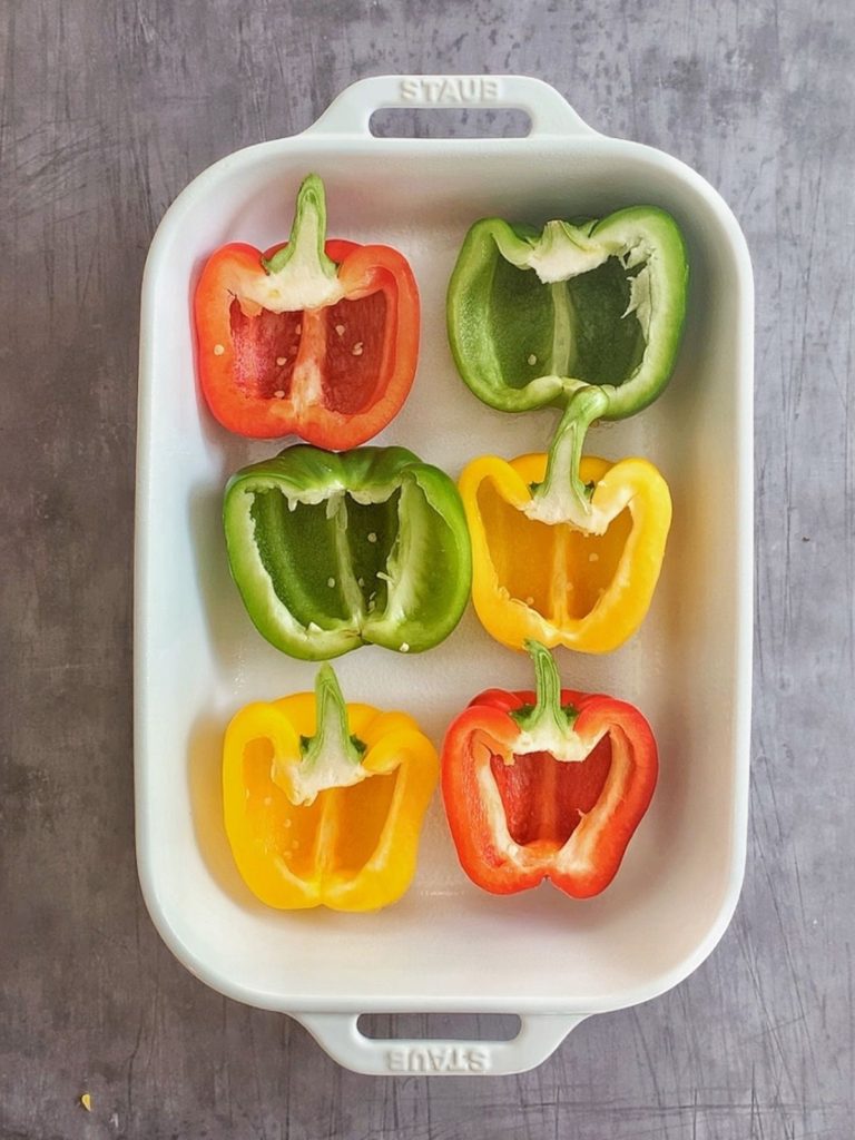 A white baking pan with 6 halves of the bell peppers cleaned and ready to be stuffed.