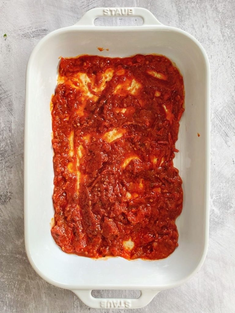 A pan with marinara sauce spread evenly across the bottom.