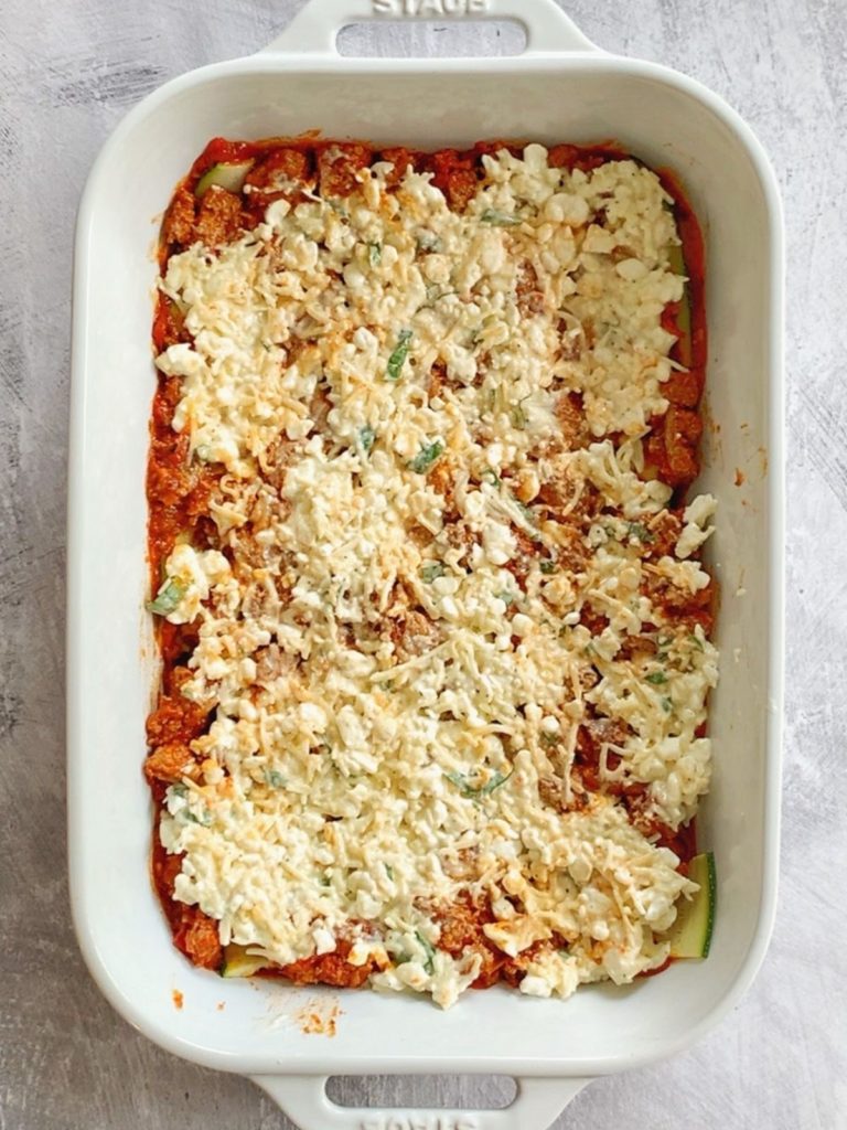 Cottage cheese mixture layered on top of meat sauce and zucchini in a pan.