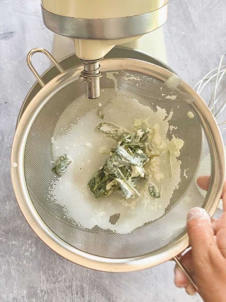 Wilted mint leaves being strained out of the milk mixture.