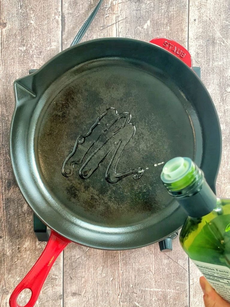 Avocado oil being drizzled into a cast iron skillet.