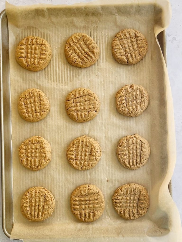 Almond flour peanut butter cookies baked and cooling on a sheet pan.