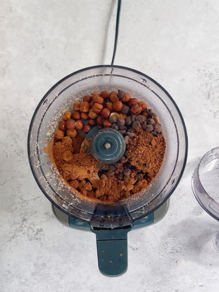 A food processor with all the ingredients needed to make chocolate hazlenut balls.