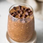 A glass of chocolate overnight oats topped with chocolate chips.
