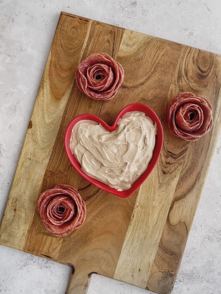 Chocolate fruit dip and salami roses on a wooden charcuterie board.
