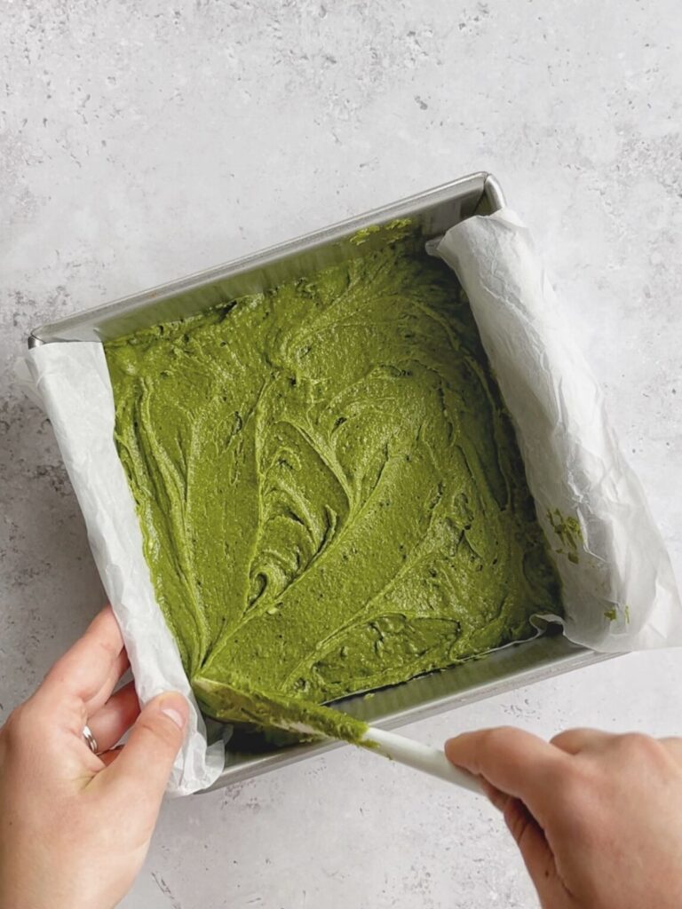 The matcha brownie batter being spread in a baking pan.