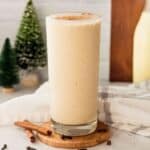 close up of eggnog shake in a clear glass with mini bottle brush trees in the background.