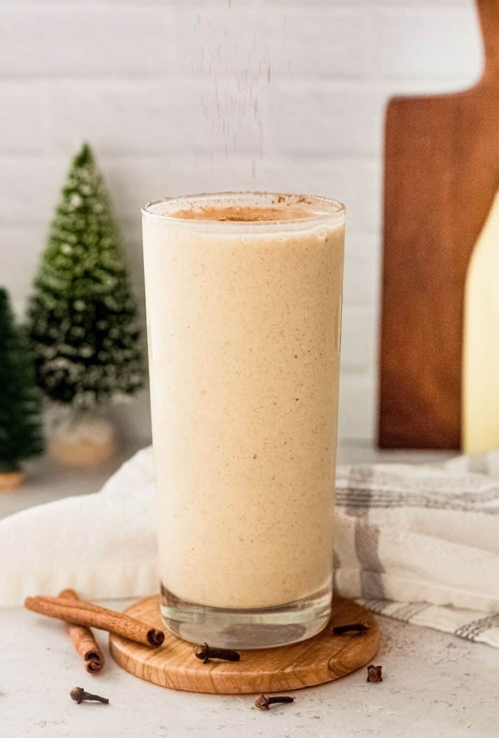 hero shot of eggnog milkshake in tall clear glass dusted with extra cinnamon.