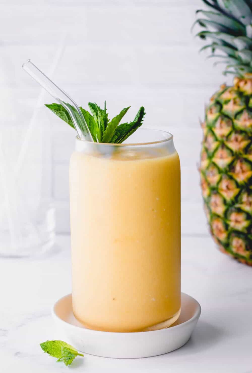A mango pineapple smoothie topped with mint leaves and a straw.