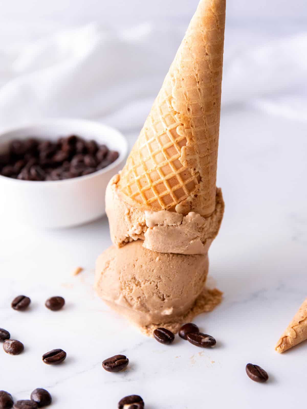 hero shot of coffee ice cream with two scoops on a cone that has been inverted on a table.