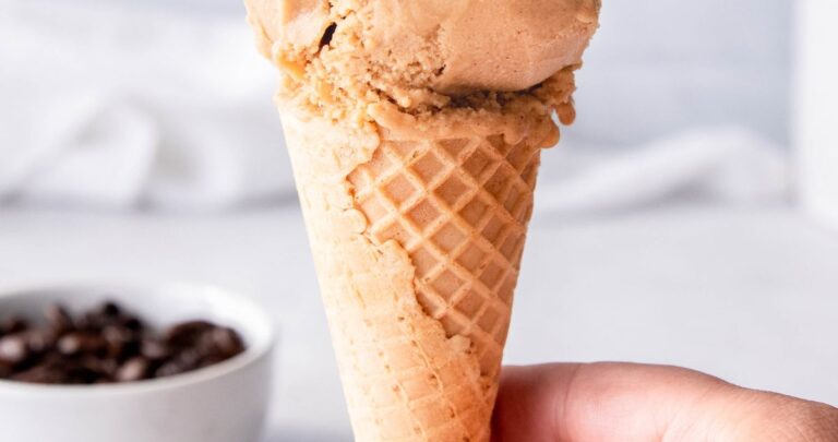 sugar cone with a scoop of coffee ice cream in front of a table scattered with coffee beans.
