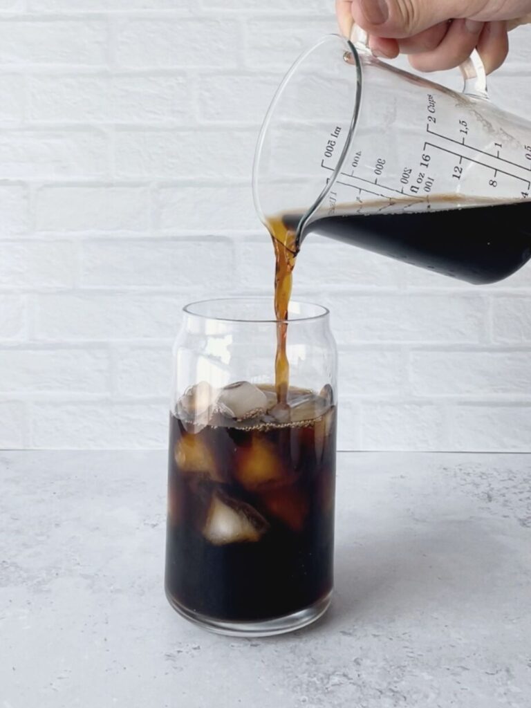 hand pouring cold brew coffee into a glass with ice.