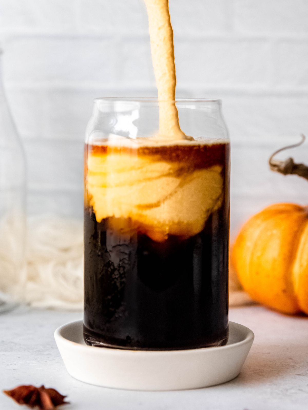 action shot of pumpkin cream cold foam being poured into a glass of cold brew coffee on ice.