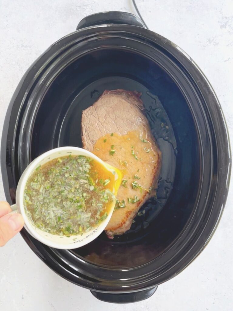 pouring the gravy liquid over the seared London broil in the crock pot.