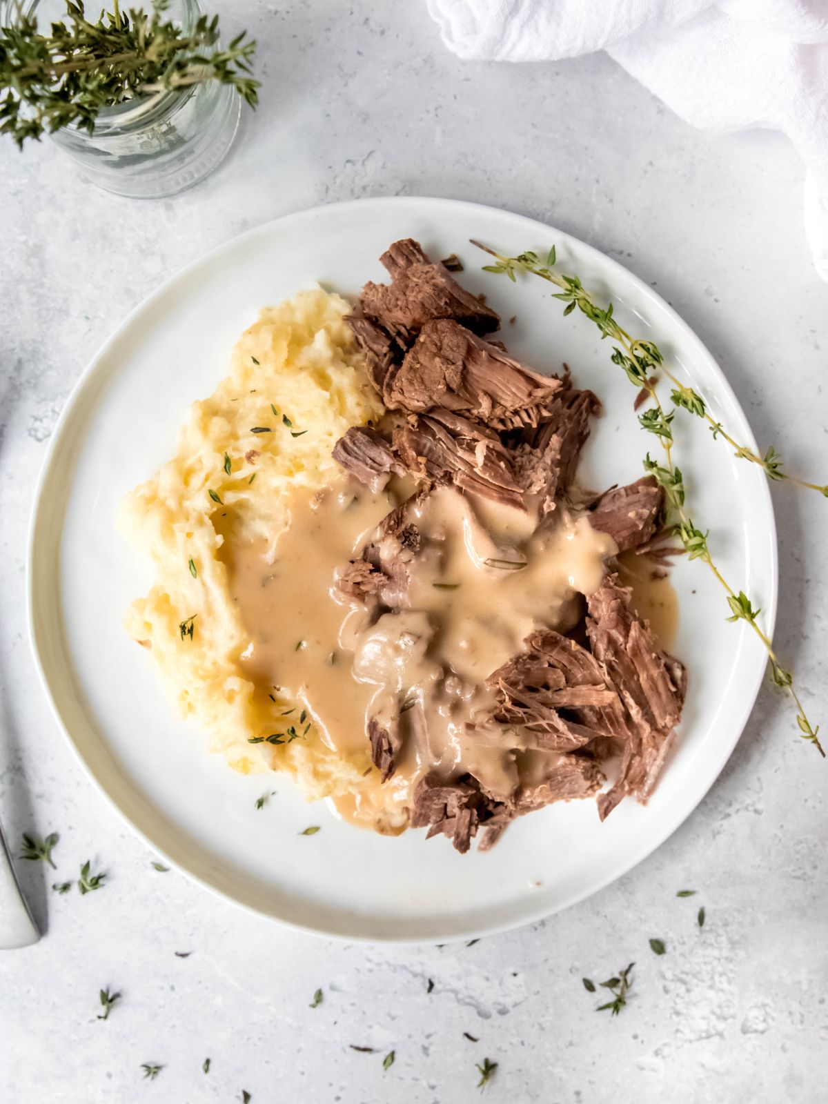 overhead shot of a white round plate with shredded slow cooker london broil, mashed potatoes, and herbed gravy.