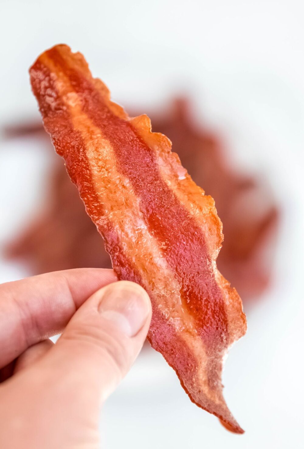 hand holding up a piece of air fryer turkey bacon to show the crisp consistency.