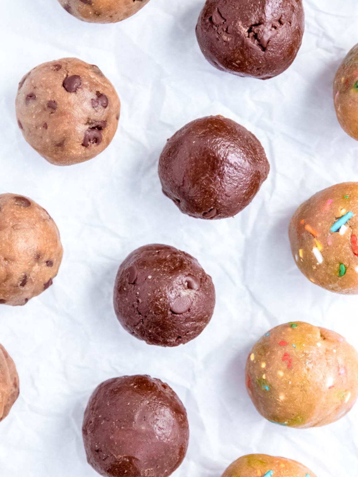 overhead shot of 3 rows of different flavored protein cookie dough balls on a piece of parchment paper.