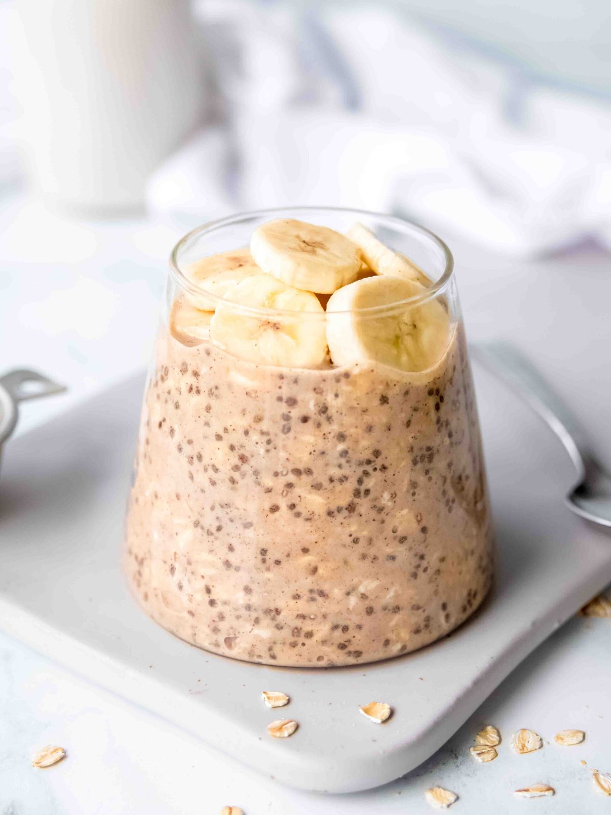 sideways hero shot of peanut butter protein overnight oats in a glass on top of a rectangular grey plate with a silver spoon.