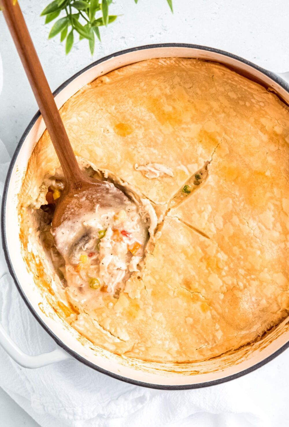 overhead shot of chicken pot pie in a dutch oven with a wooden spoon sticking out of it and a portion removed.