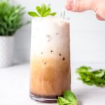side on shot of copycat Philz coffee mint mojito in a clear glass with a hand stirring the glass straw.