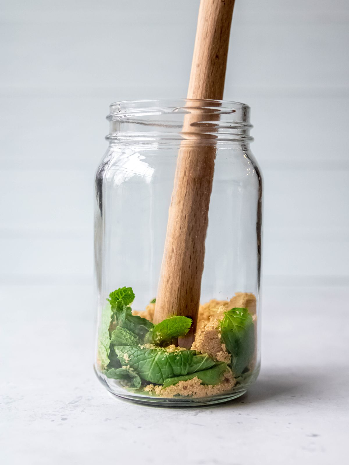 wooden muddling stick crushing the mint leaves into the brown sugar.