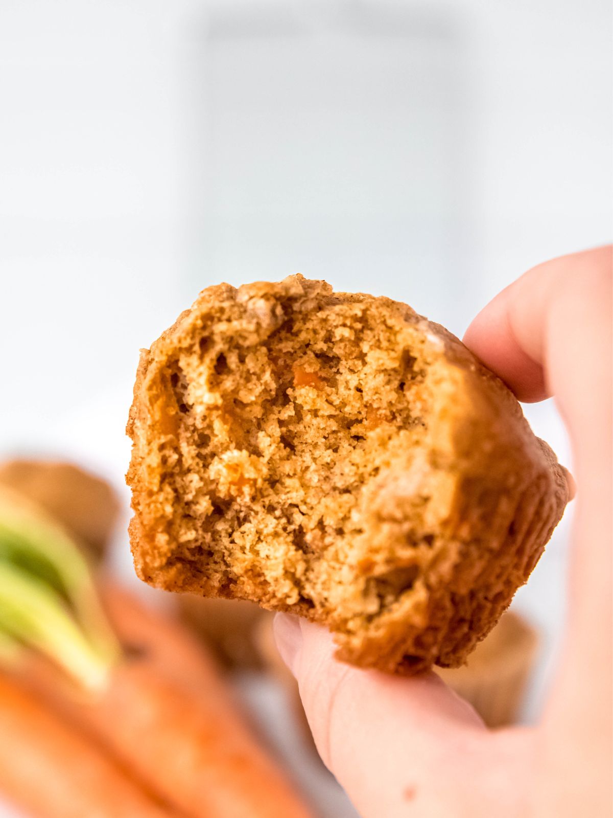 side on shot of a banana carrot muffin with a bite taken out to show the tender crumbed interior.
