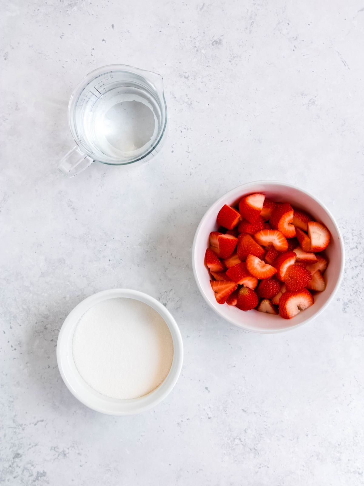 ingredients needed to make strawberry simple syrup measured out into bowls on a white table.