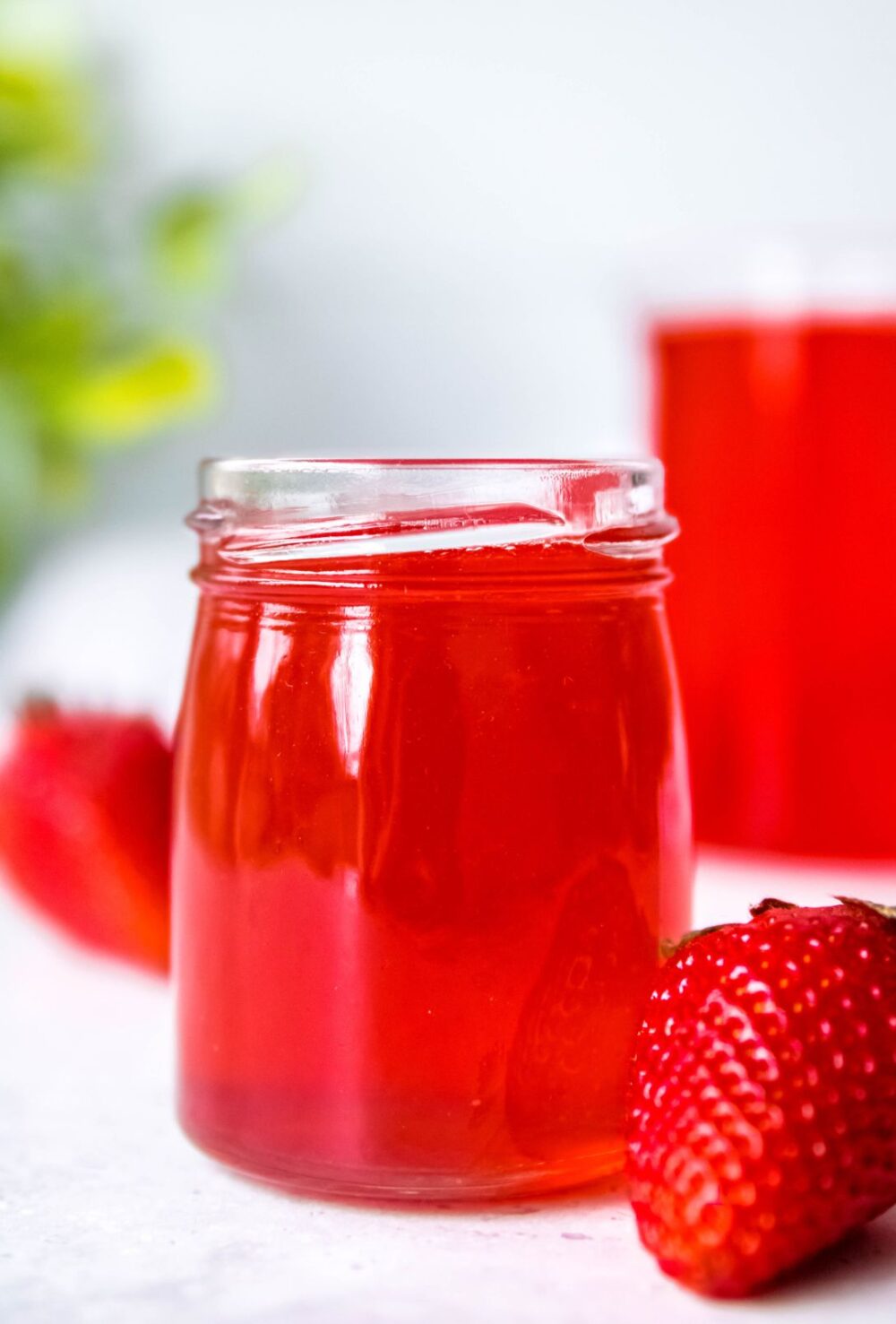 glass jar filled with strawberry simple syrup with whole strawberries scattered around.