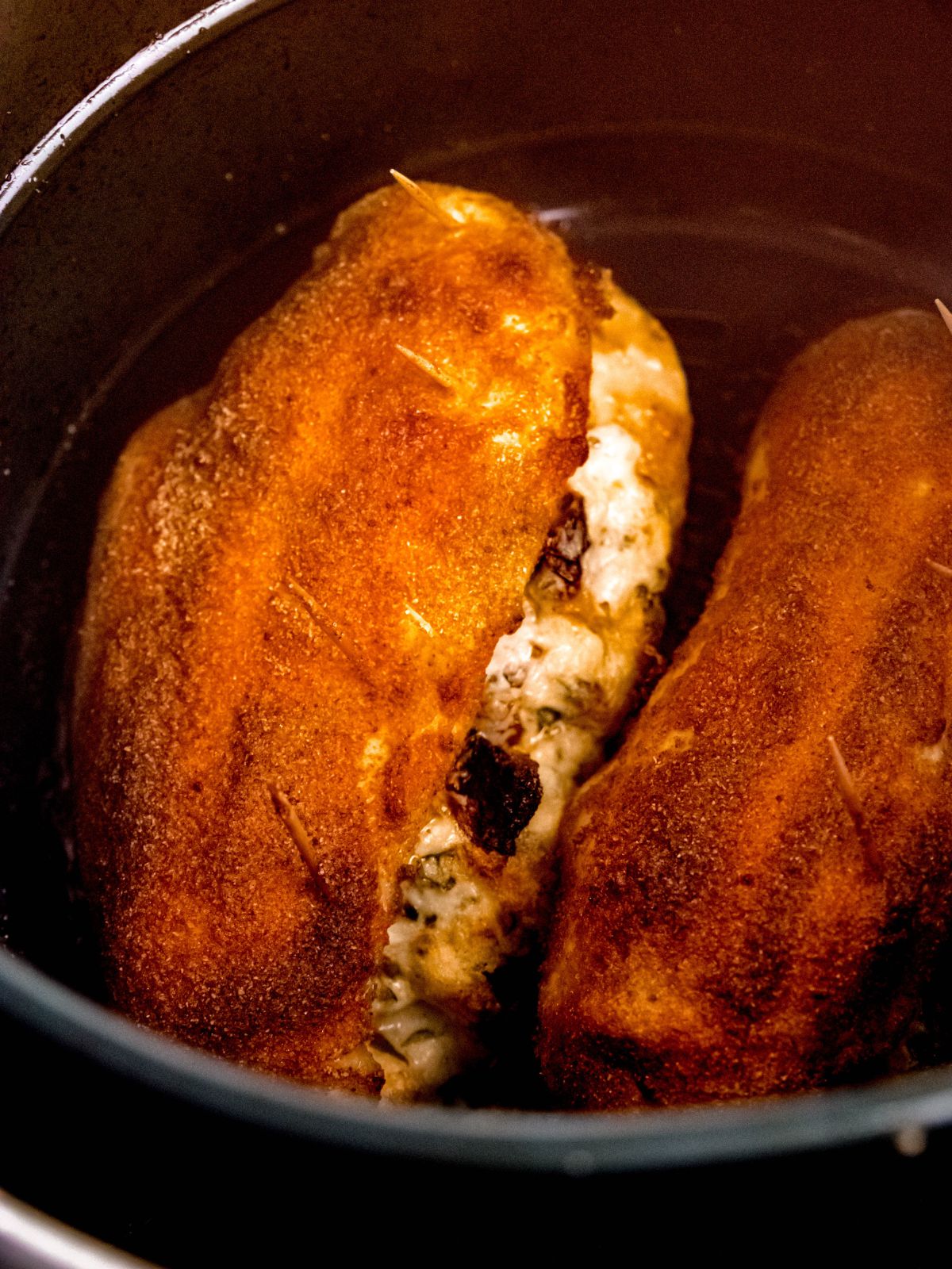 closeup shot of stuffed air fried chicken breasts in the air fryer basket showing the bubbly filling.