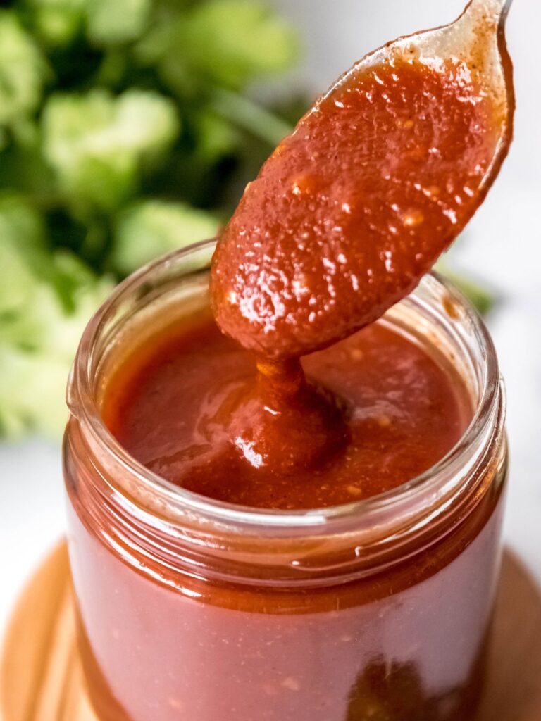 hero shot of gluten-free enchilada sauce in a clear glass jar with a silver spoon.