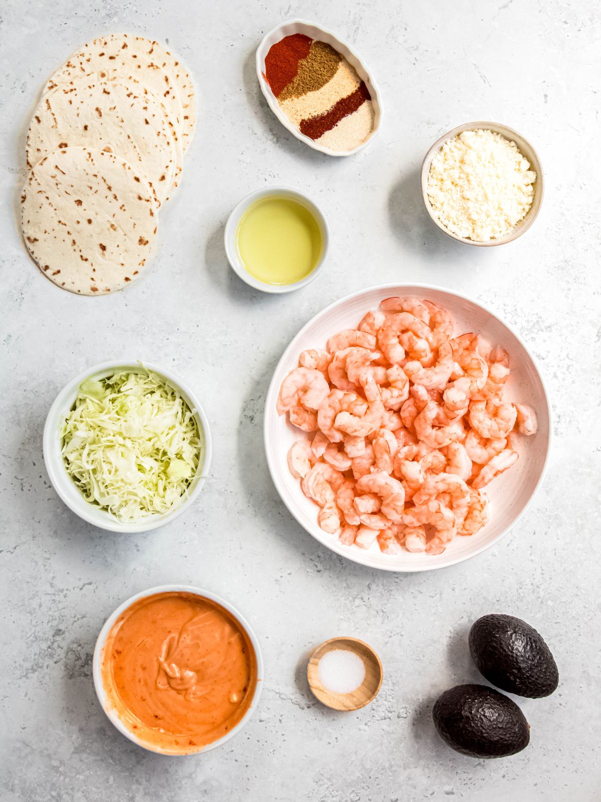 ingredients needed to make air fryer shrimp tacos measured out into bowls on a white table.