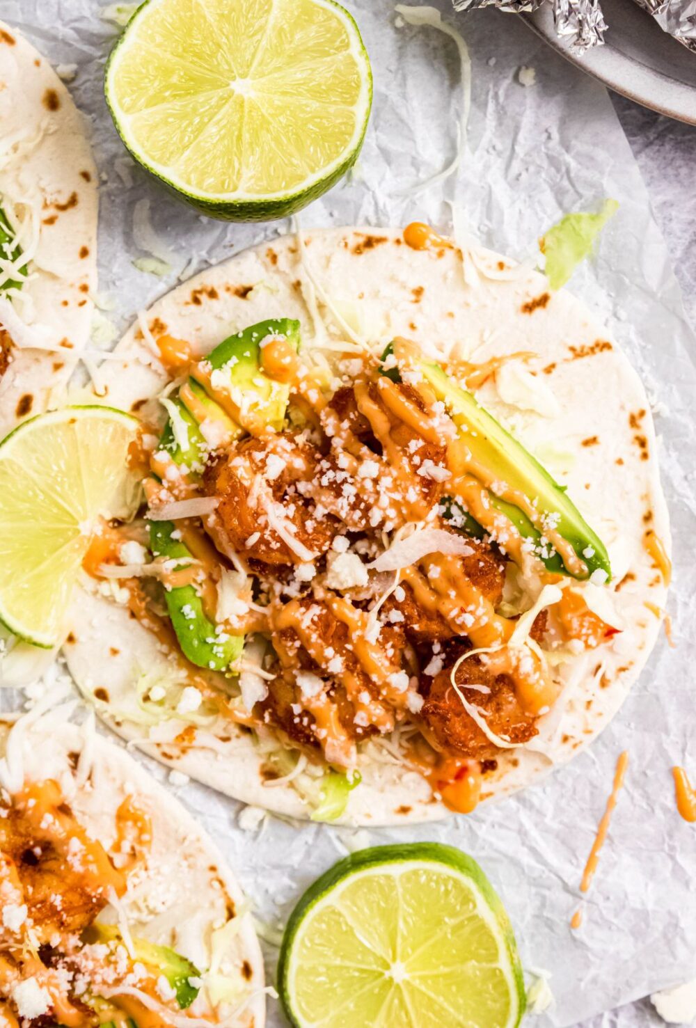 closeup flatlay shot of a juicy, spicy air fryer shrimp taco drizzled with bang bang sauce and with lime wedges scattered about.