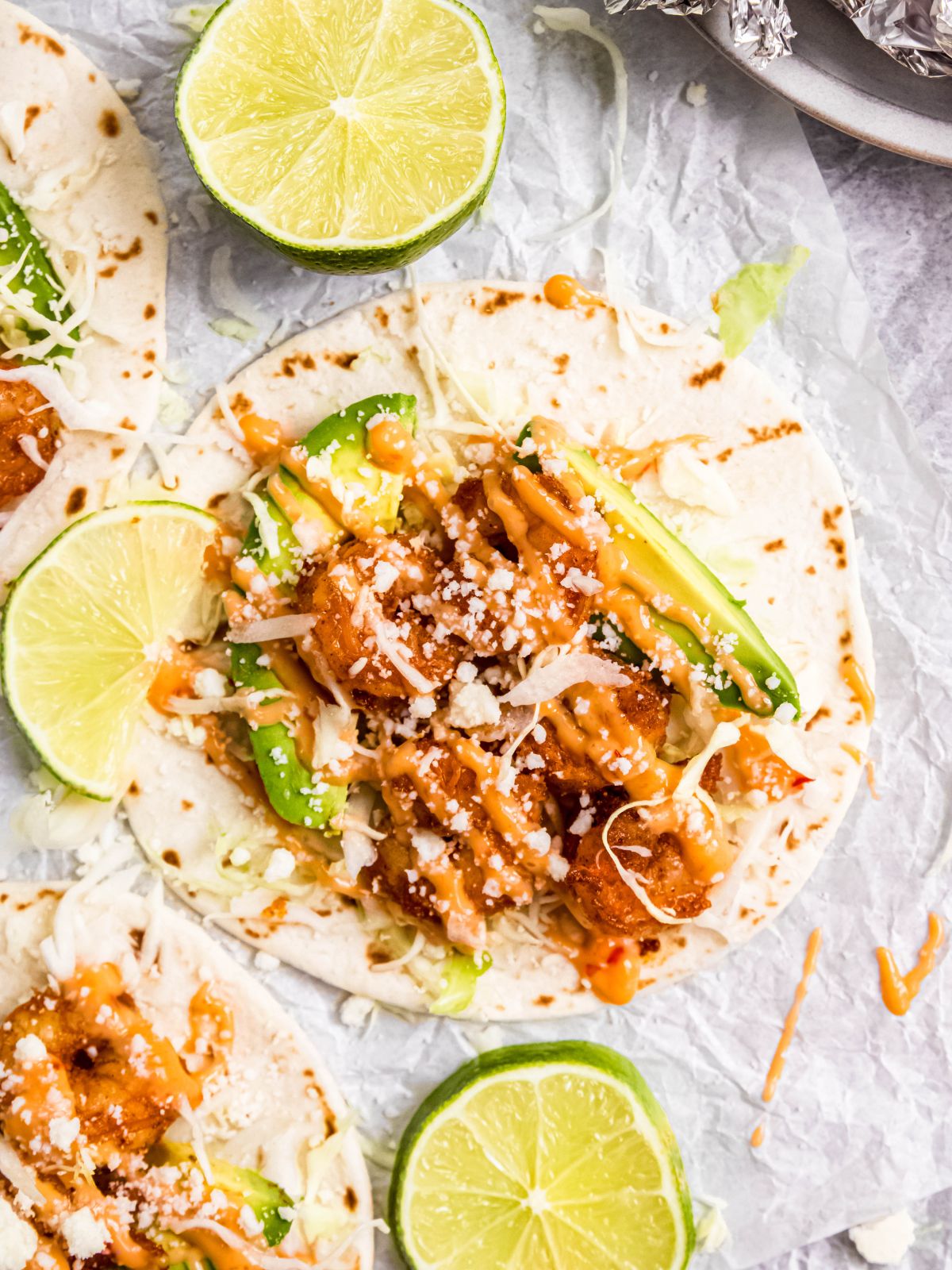 closeup flatlay shot of a juicy, spicy air fryer shrimp taco drizzled with bang bang sauce and with lime wedges scattered about.