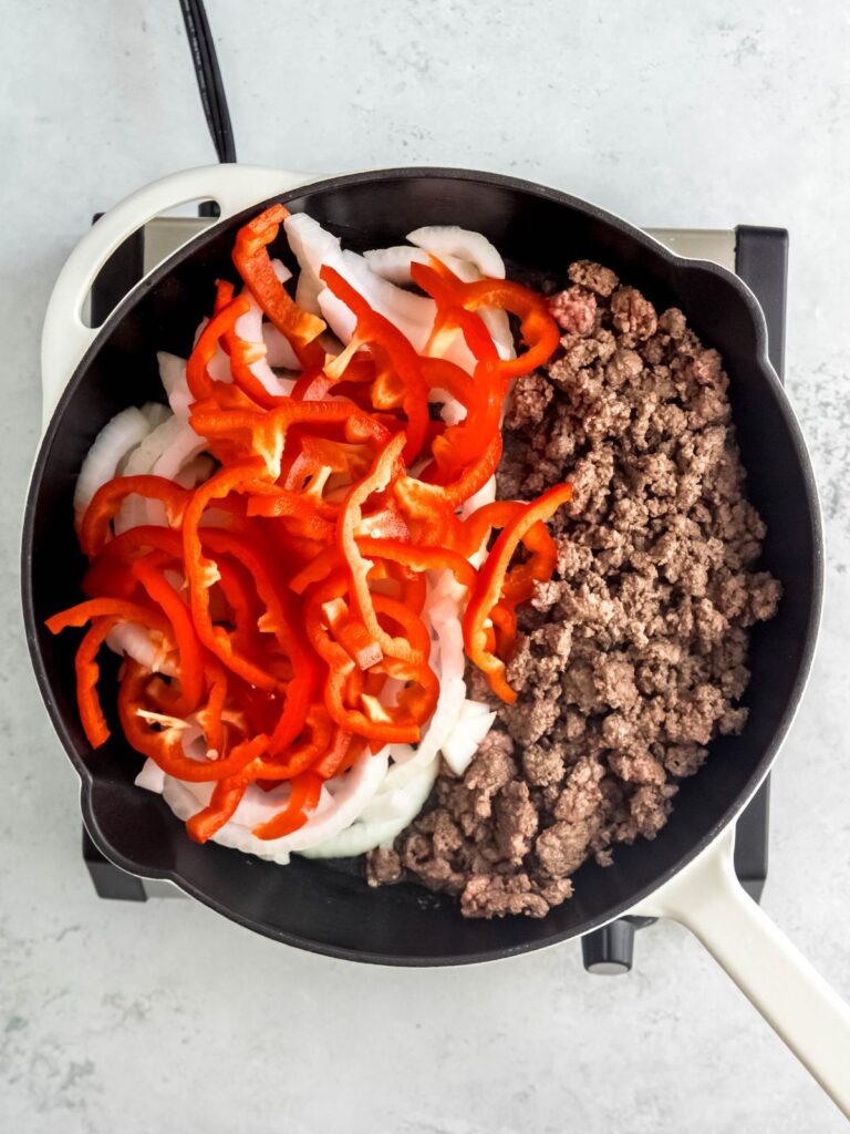 Cooked ground beef, peppers, and onions in a skillet.