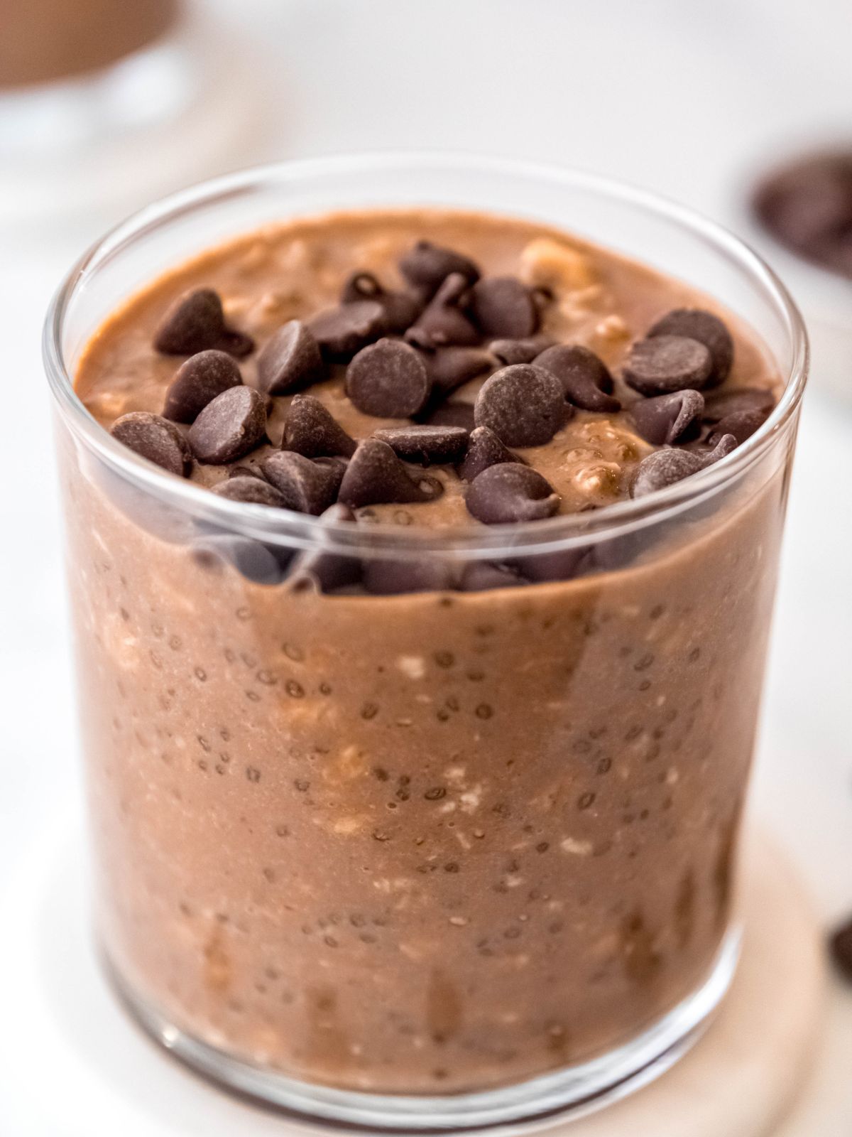 45 degree angle shot of a clear glass of chocolate overnight oats with peanut butter, protein powder, chia seeds, and chocolate chips.