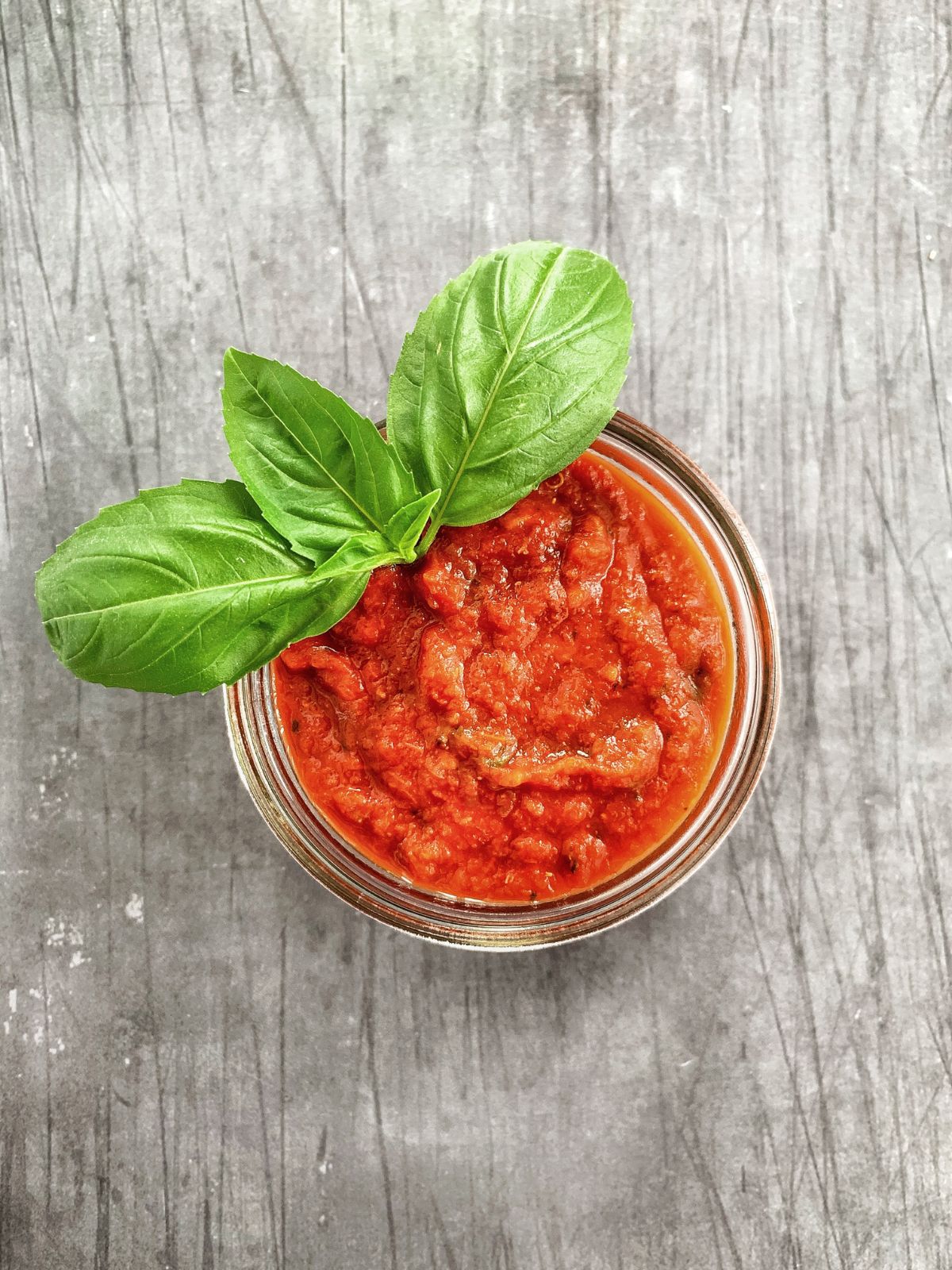 overhead shot of a mason jar of marinara pizza sauce on a grey table.