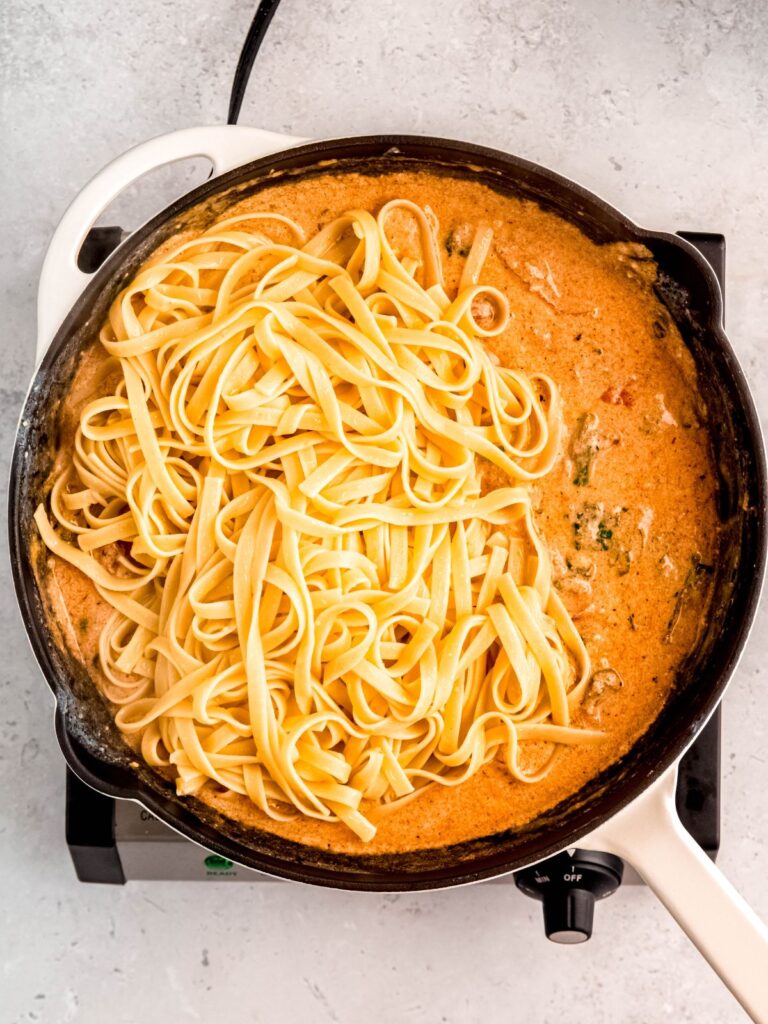 A pot of Cajun alfredo sauce with cooked fettuccine on top.
