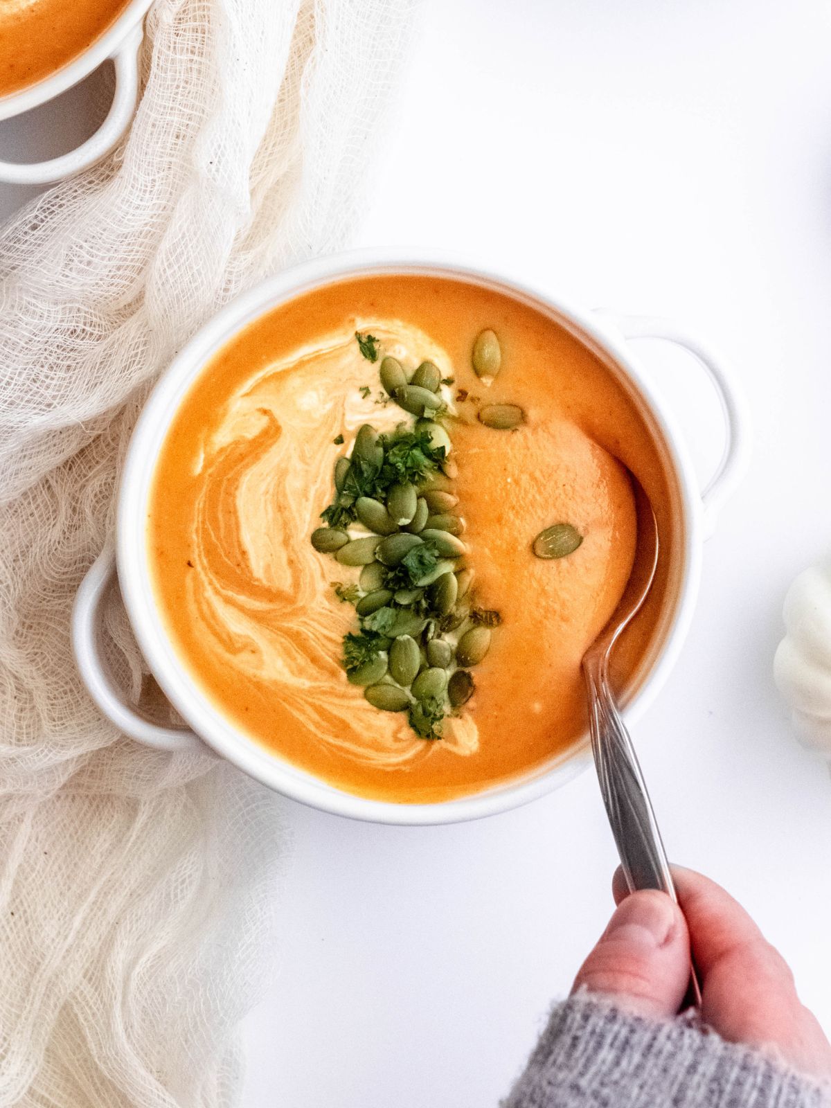 sweatered hand taking a spoonful of pumpkin curry soup garnished with pepitas and coconut milk.