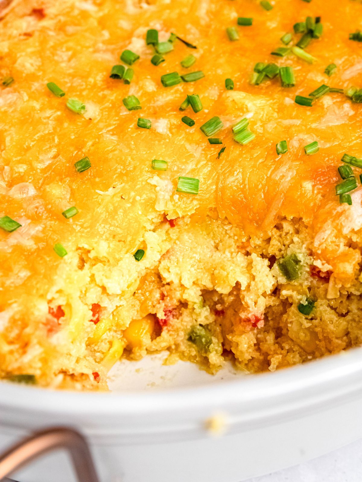 closeup shot of cheesy make-ahead healthy corn casserole in the baking pan with a scoop taken out so you can see the melty cheese layer and creamy, cornbread-like interior.