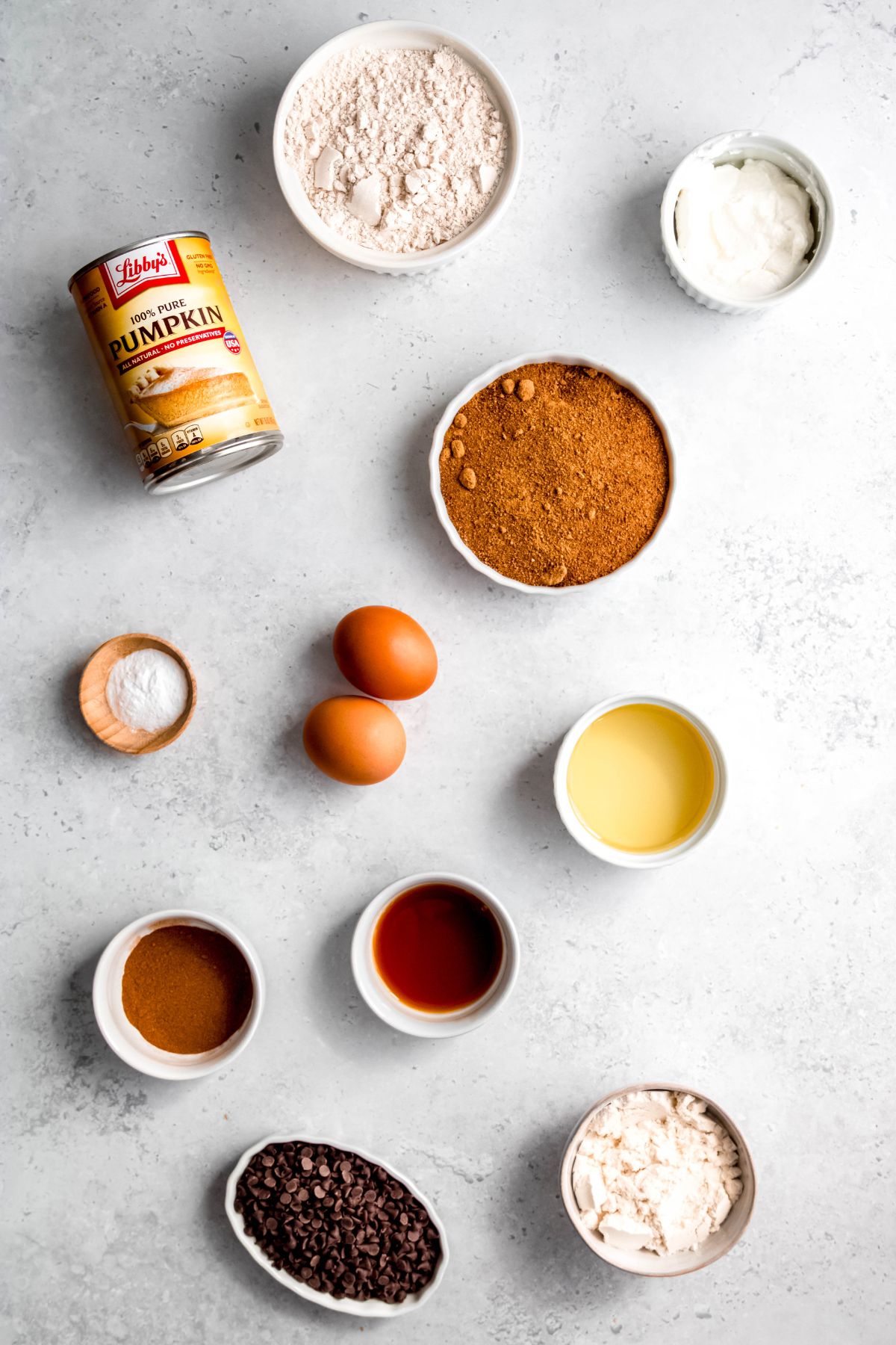 Ingredients needed to make pumpkin protein muffins measured out into bowls on a white table.